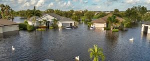 Severe flooding in the town with streets submerged; houses and cars are partially underwater.