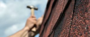 Man is holding a hammer and fixing something on the roof of the house.